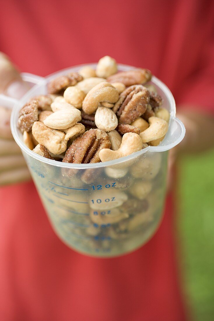 Person holding measuring jug full of mixed nuts