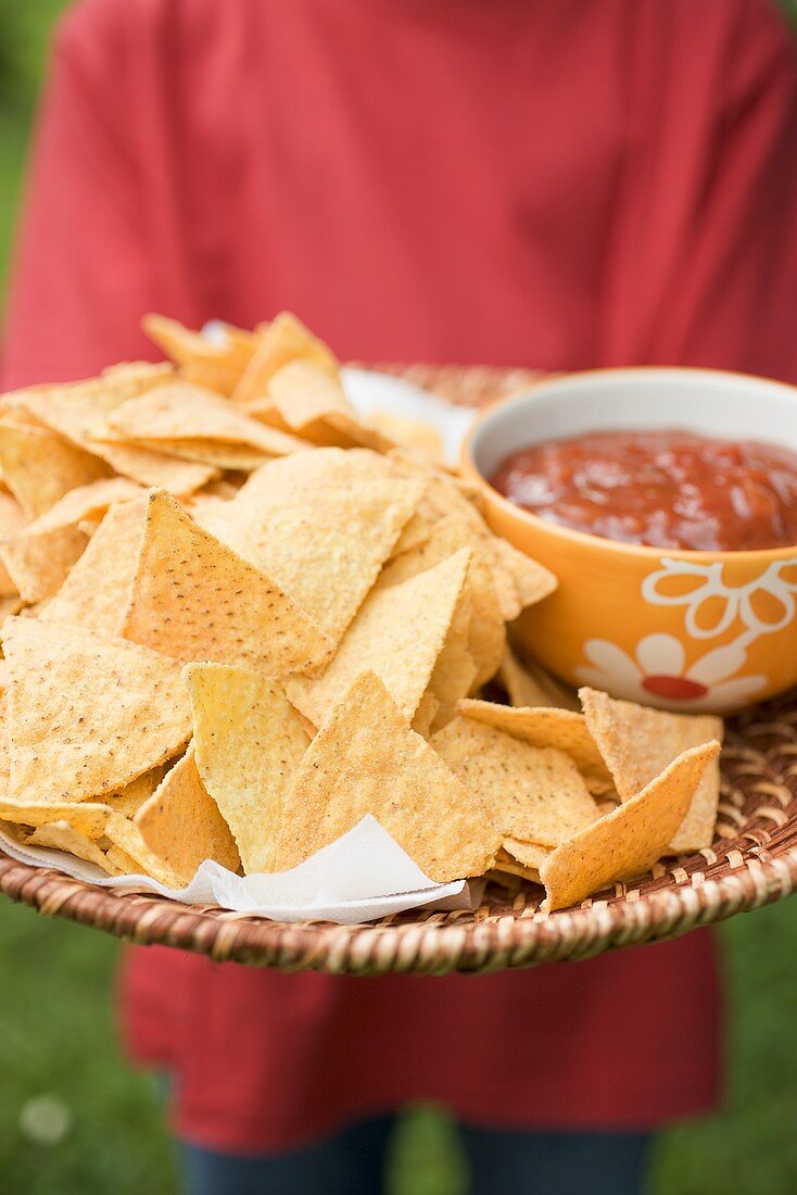 Person hält Tablett mit Nachos und Salsa