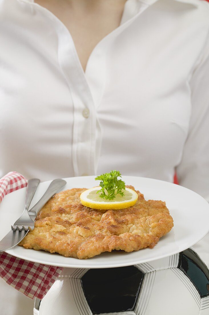 Frau hält Teller mit Wiener Schnitzel auf Fussball