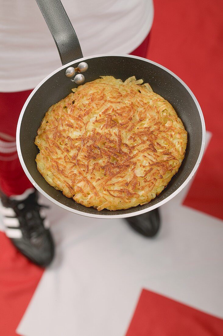 Footballer on Swiss flag holding frying pan with rösti