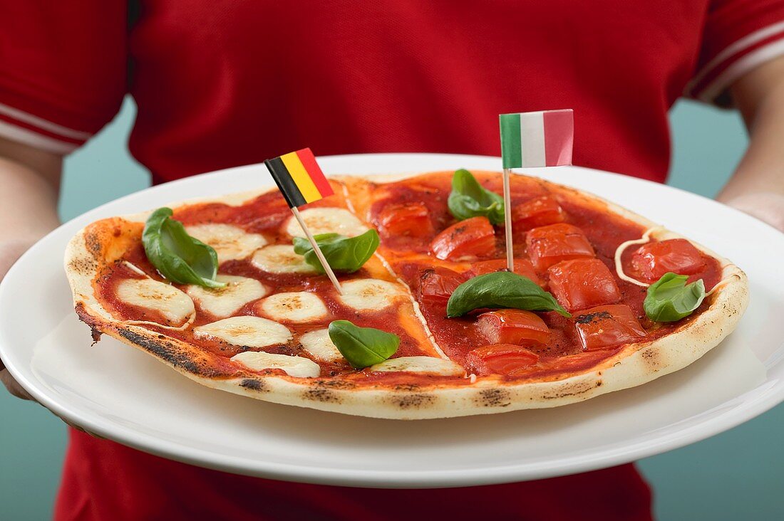 Fussballspielerin hält Tomaten-Mozzarella-Pizza mit Flaggen