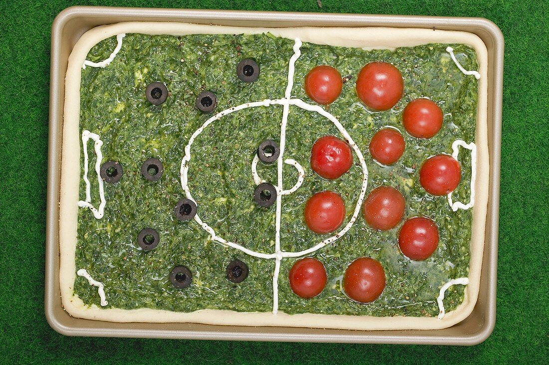 Spinach pizza with tomatoes & olives depicting a football pitch