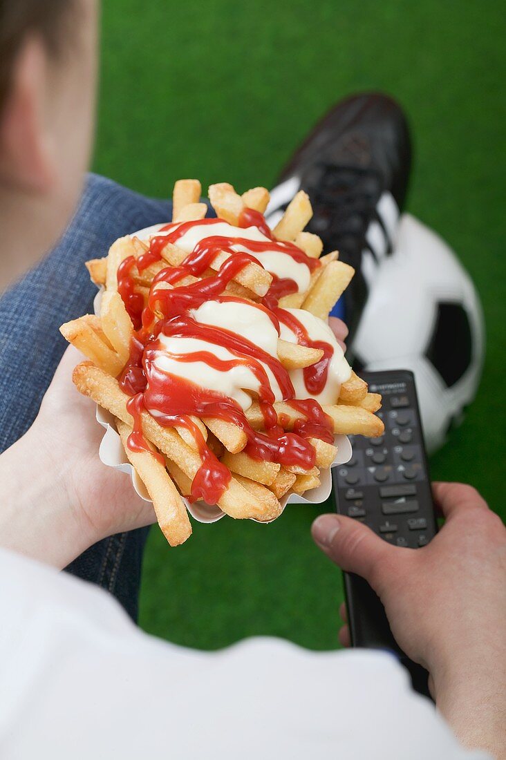 Fussballfan hält Pommes frites und Fernbedienung