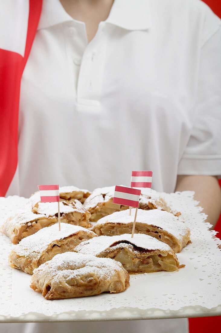 Frau hält mehrere Stücke Apfelstrudel auf Tablett (Österr.)