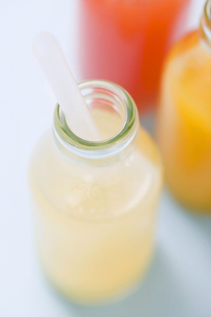 Three fruit juices in bottles with straws