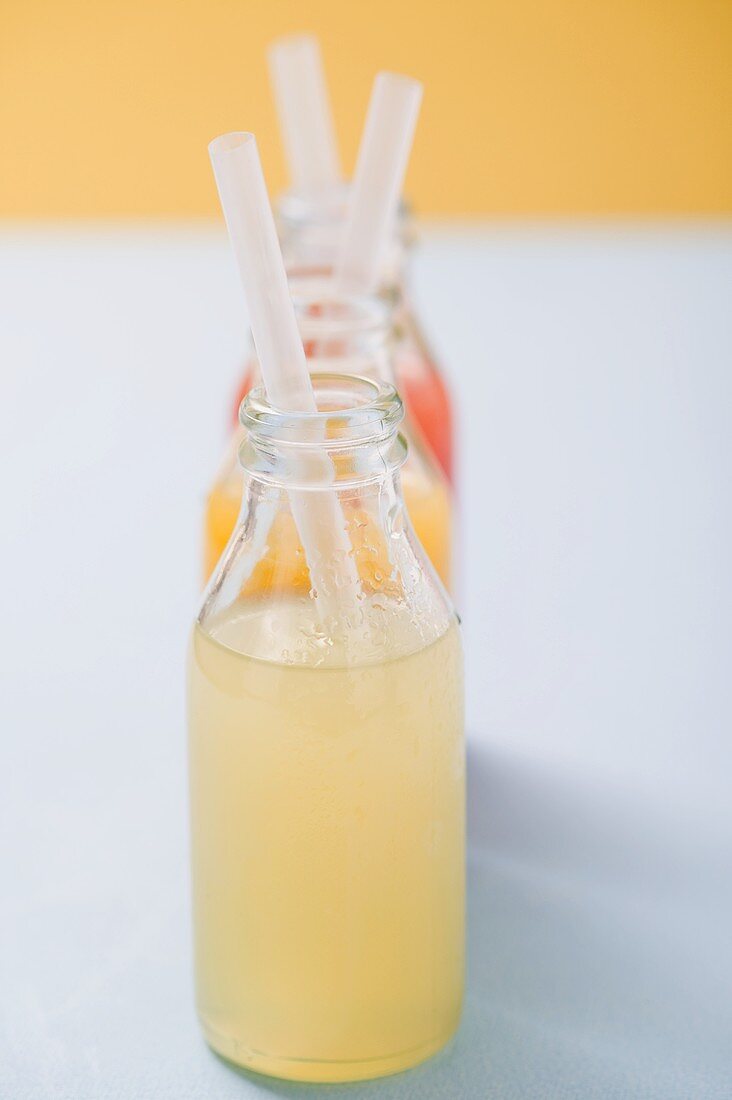 Three fruit juices in bottles with straws