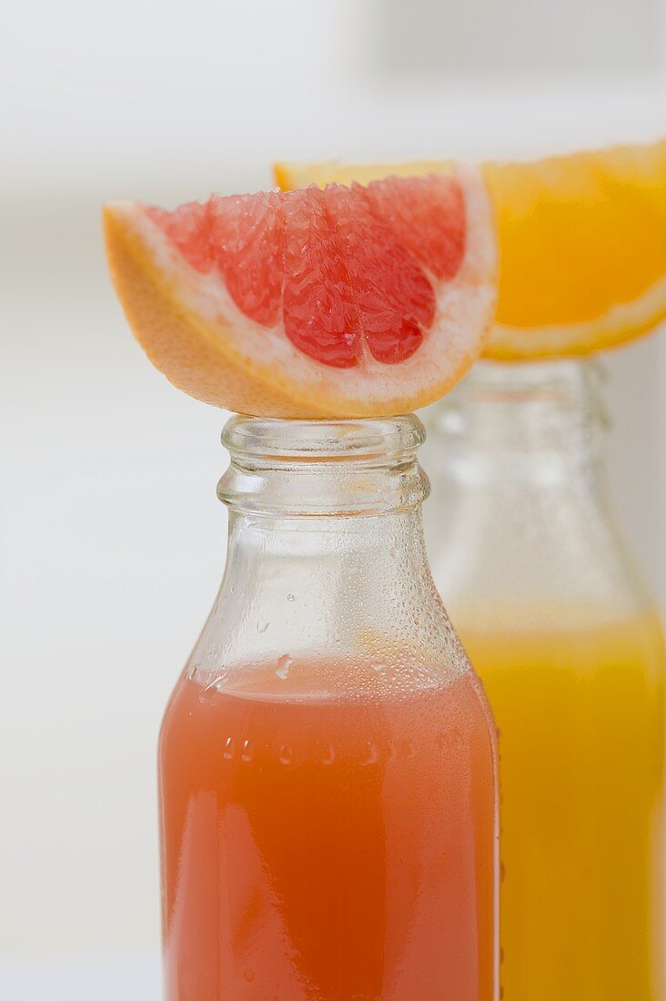 Three fruit juices in bottles with wedges of fresh fruit