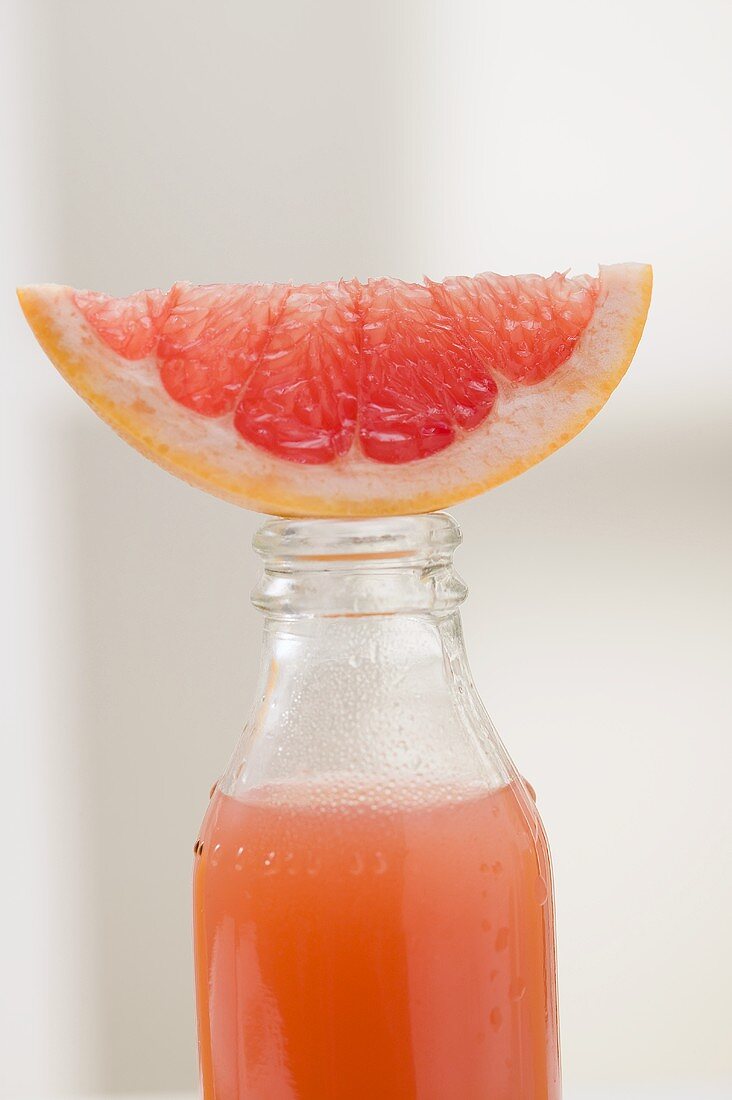 Pink grapefruit juice in bottle with fresh grapefruit wedge