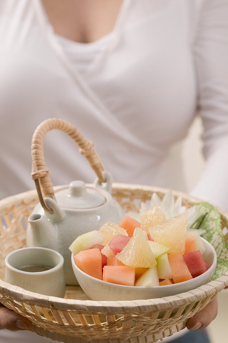 Frau hält Korb mit Tee und Fruchtsalat