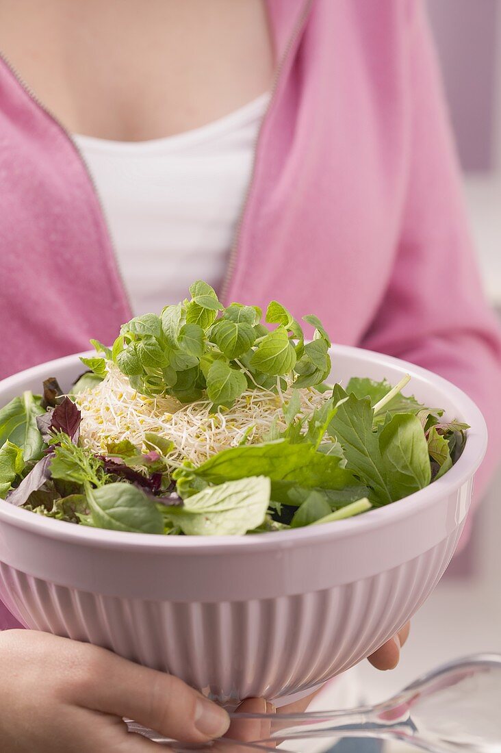 Frau hält Schüssel mit Blattsalat und Sprossen