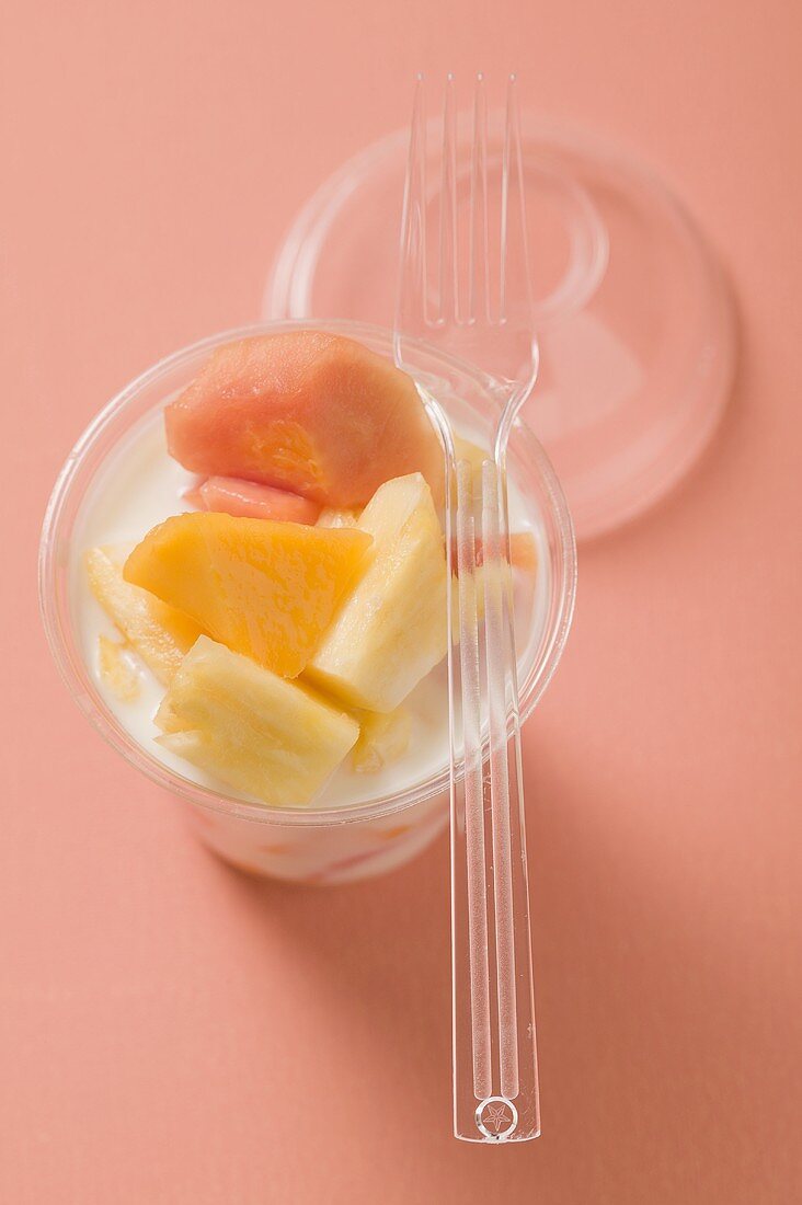 Joghurt mit frischen Früchten im Plastikbecher, darauf Gabel
