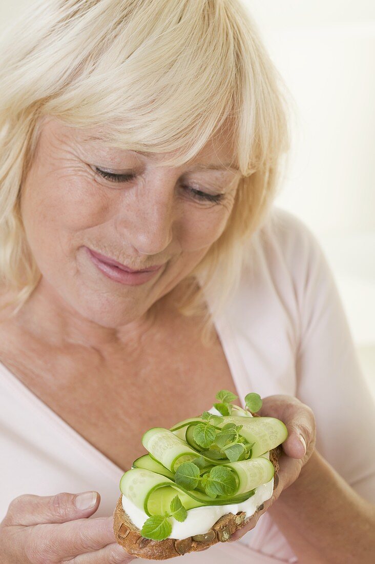 Woman holding slice of bread with yoghurt & cucumber slices