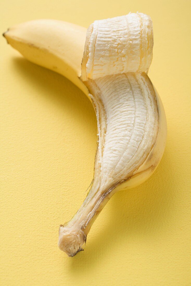 Banane, halb geschält, auf gelbem Untergrund