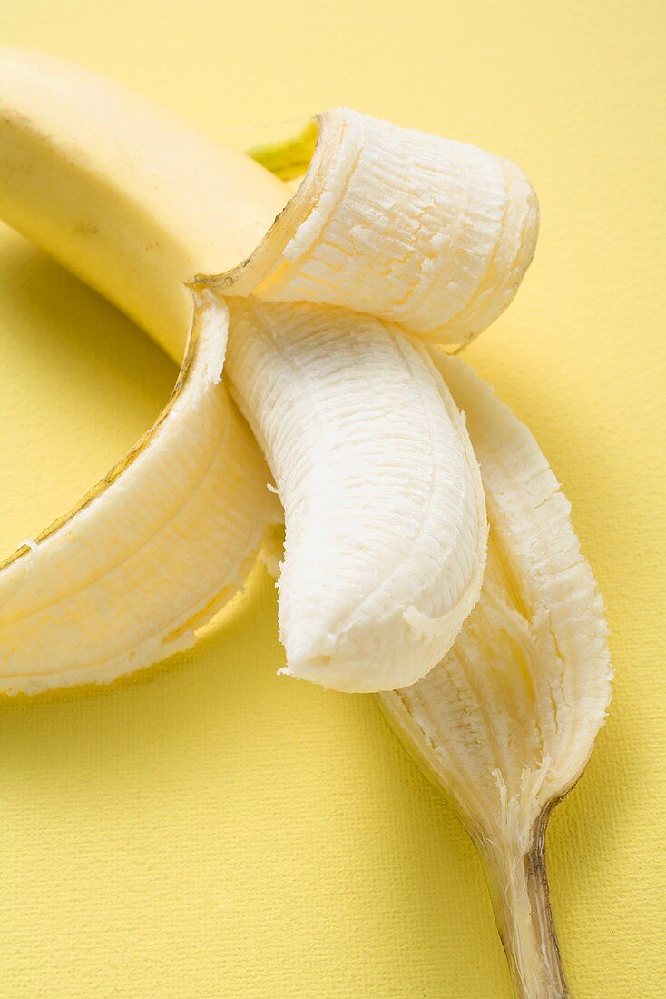 Banana, half peeled, on yellow background