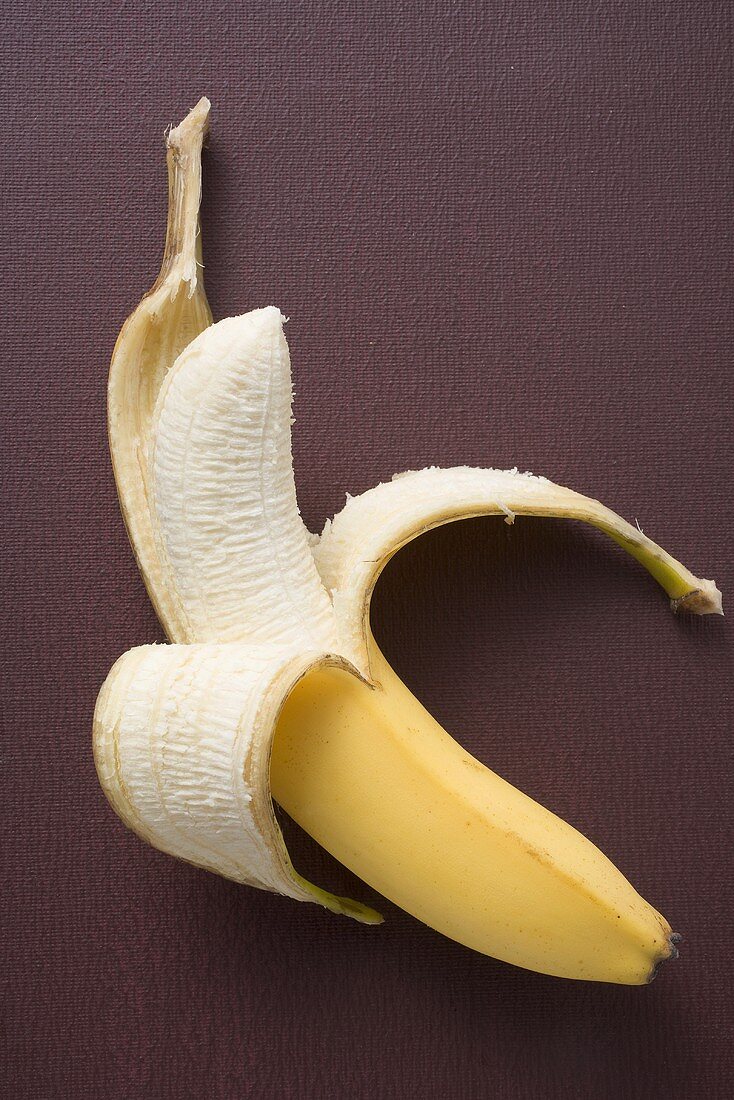 Banana, half peeled, on brown background