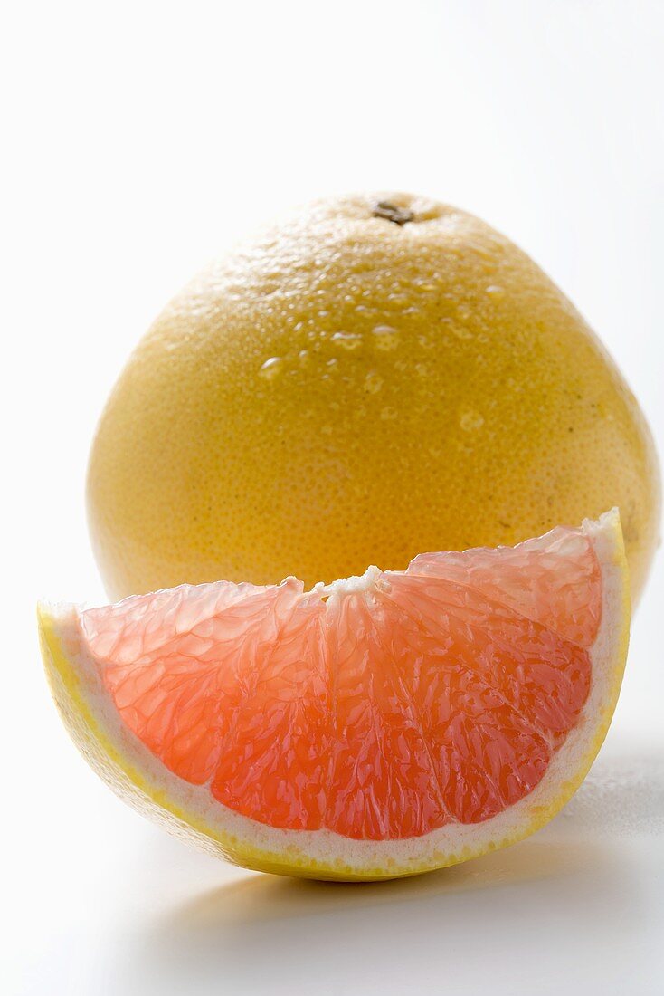 Wedge of pink grapefruit in front of whole grapefruit