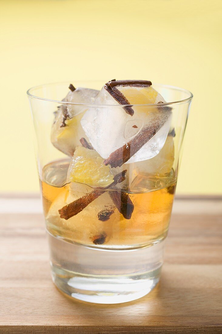 Rum und Eiswürfel mit Gewürzen und Fruchtstücken im Glas