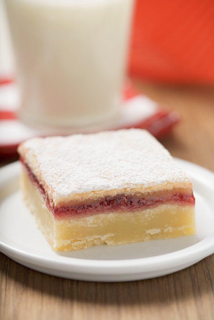 Jam slice with icing sugar on plate in front of glass of milk