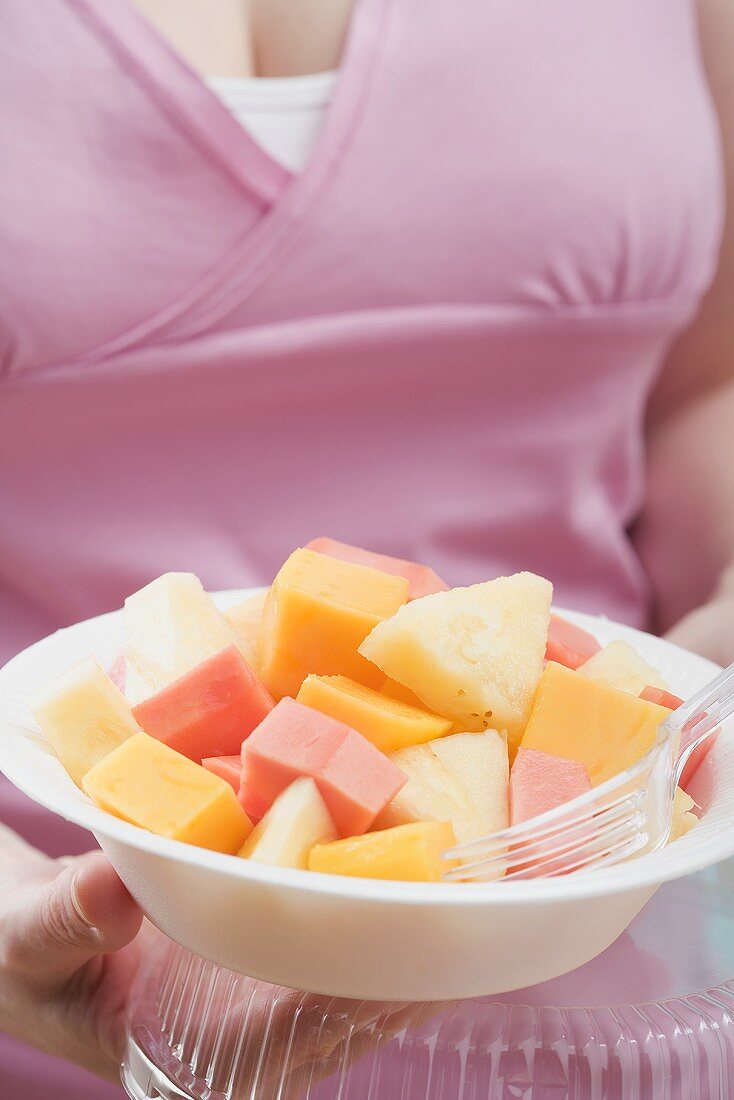 Frau hält exotischen Fruchtsalat auf Plastikteller