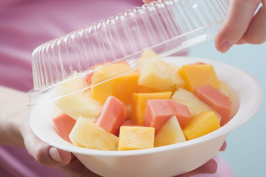 Woman removing lid from plastic dish of exotic fruit salad