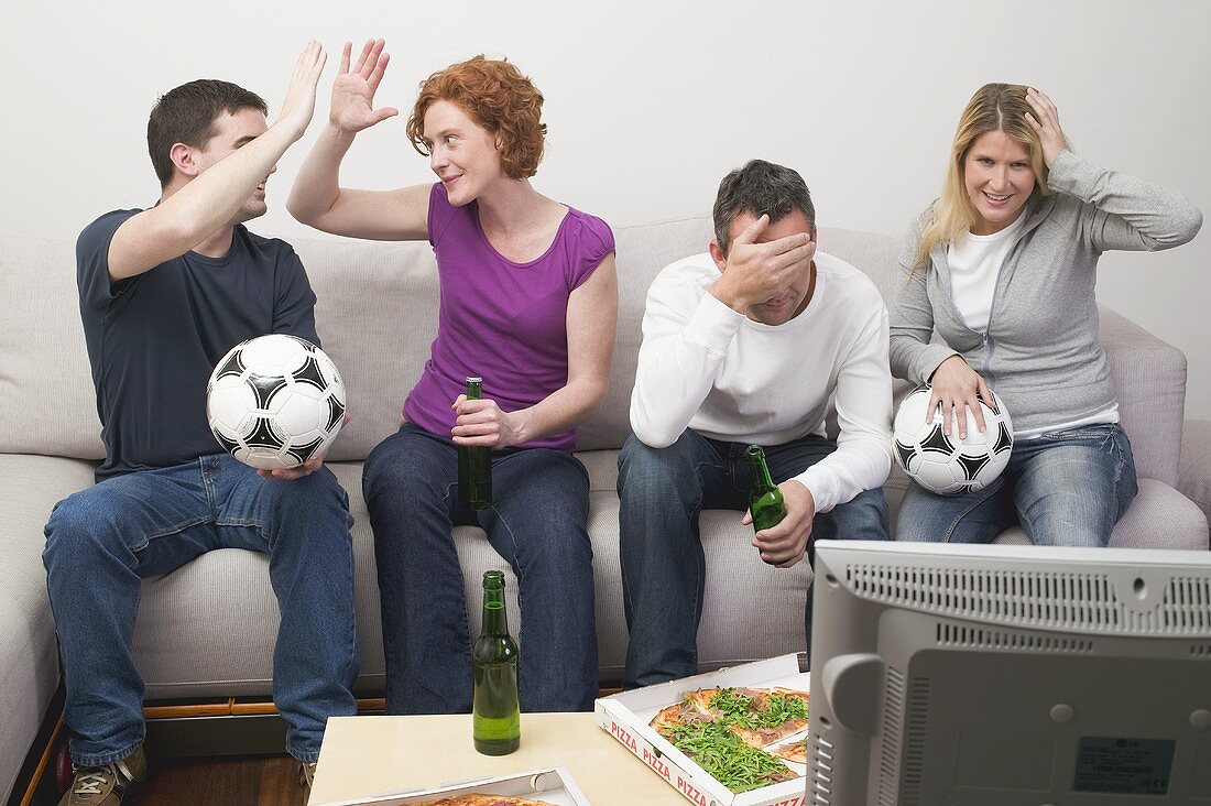 Friends in front of TV with footballs, beer and pizza