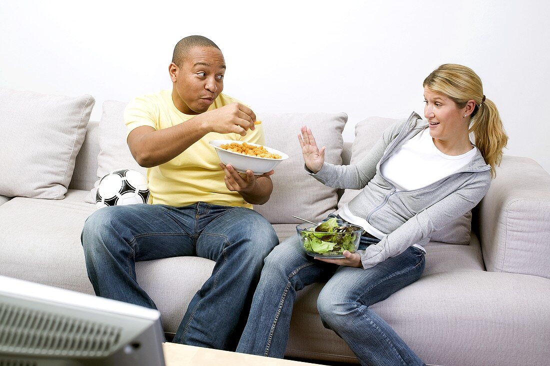 Couple with peanut puffs and salad in front of TV