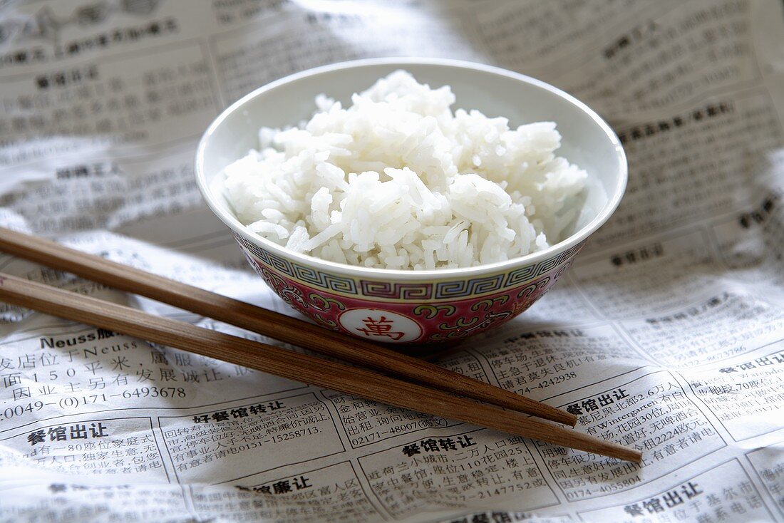 Reis in chinesischer Schale auf Zeitung, daneben Essstäbchen