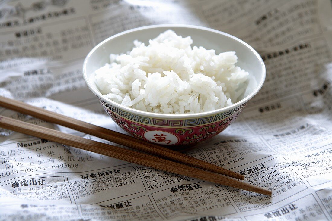 Rice in Asian bowl on newspaper, chopsticks beside it