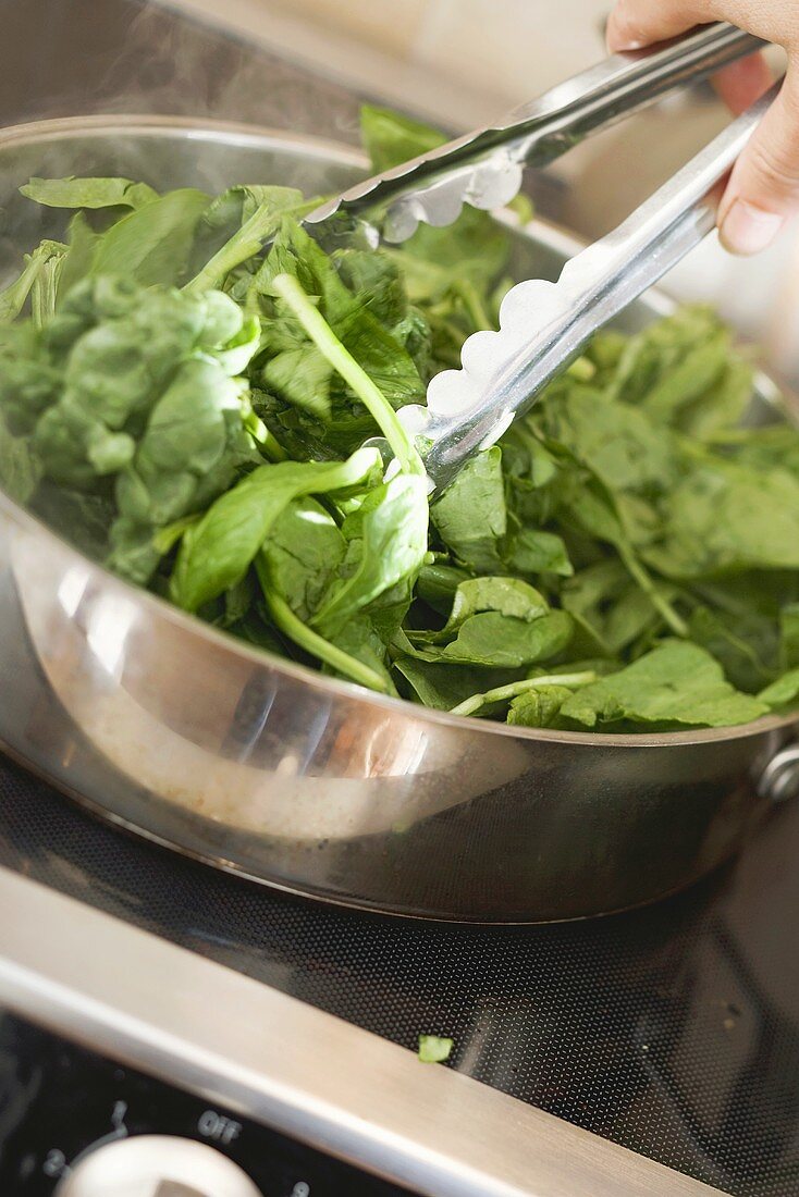 Turning spinach in pan with tongs