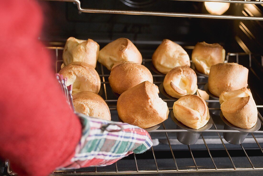 Hand taking freshly baked popovers out of oven