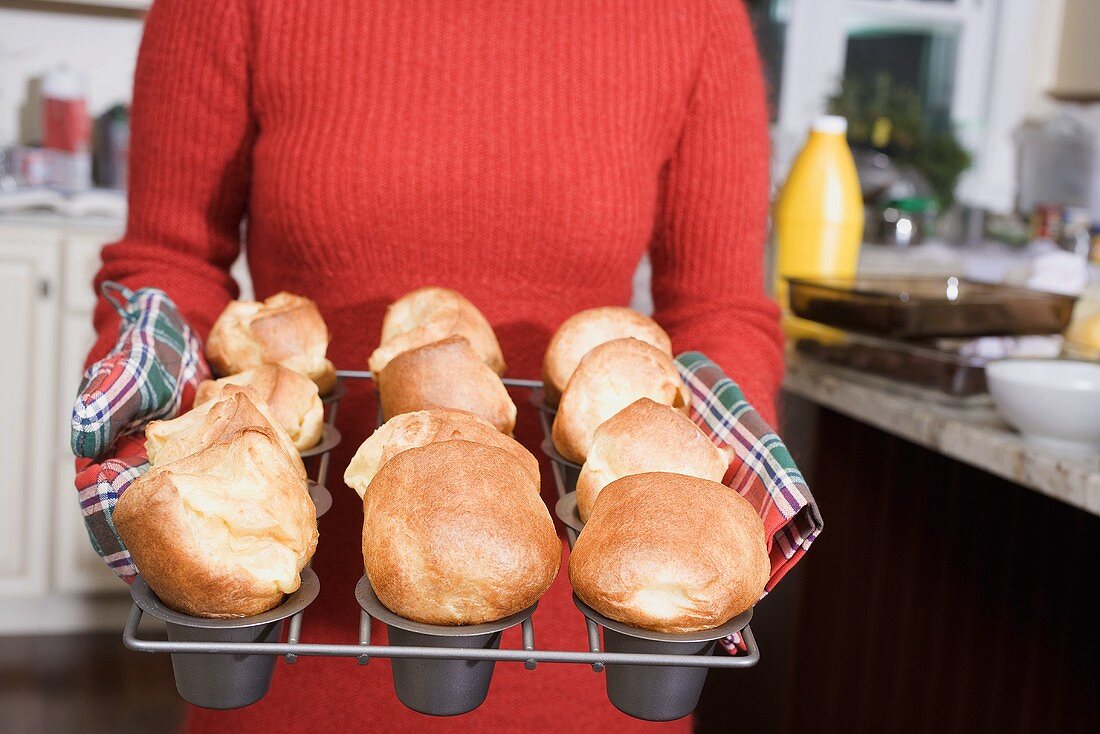 Woman holding freshly baked popovers on a rack