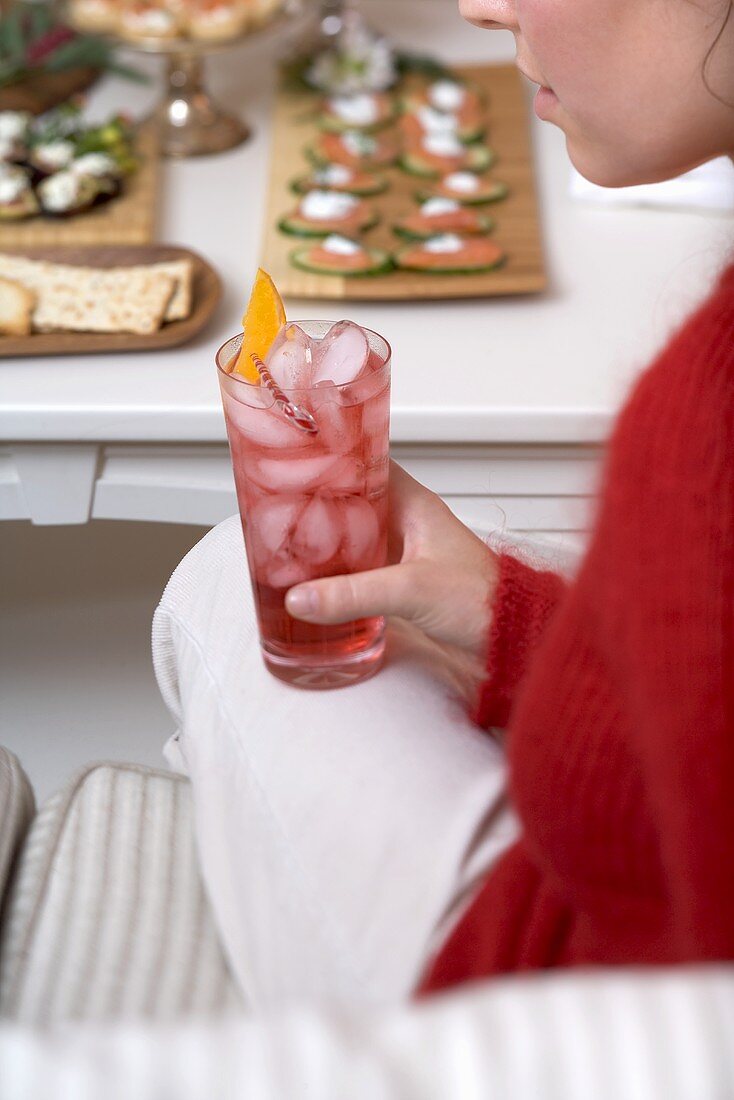 Woman holding glass of Campari with ice cubes, snacks in background