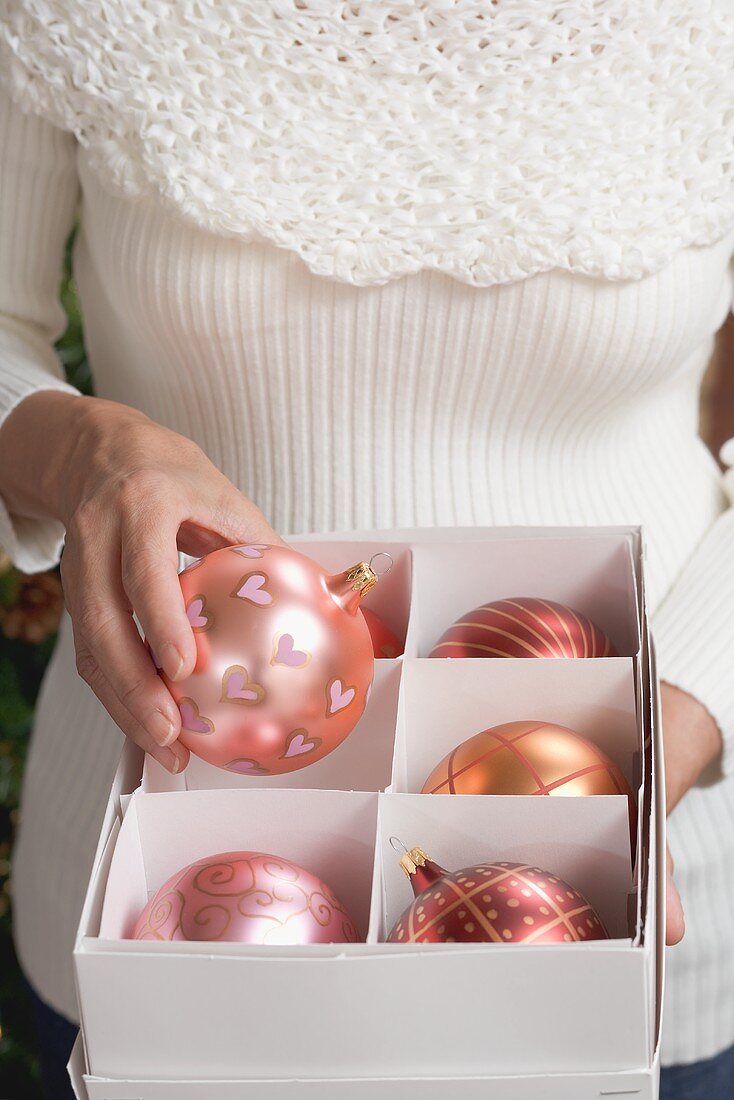 Frau nimmt rosa Christbaumkugel aus Schachtel