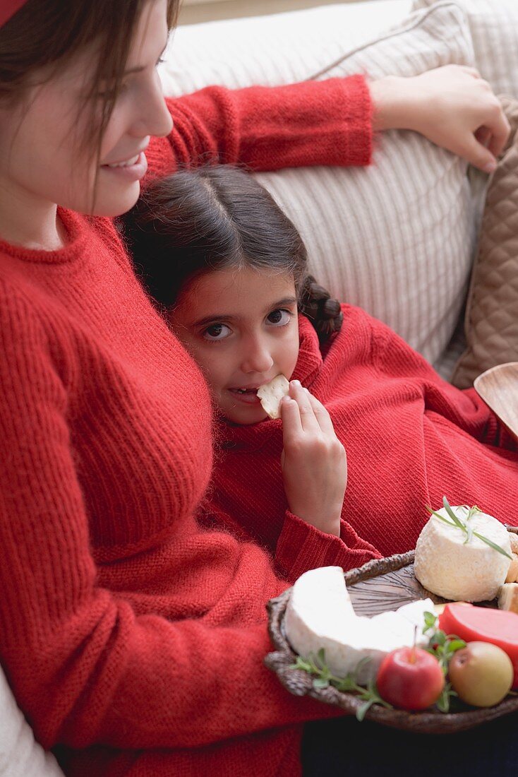 Woman and girl on sofa with cheeseboard and crackers