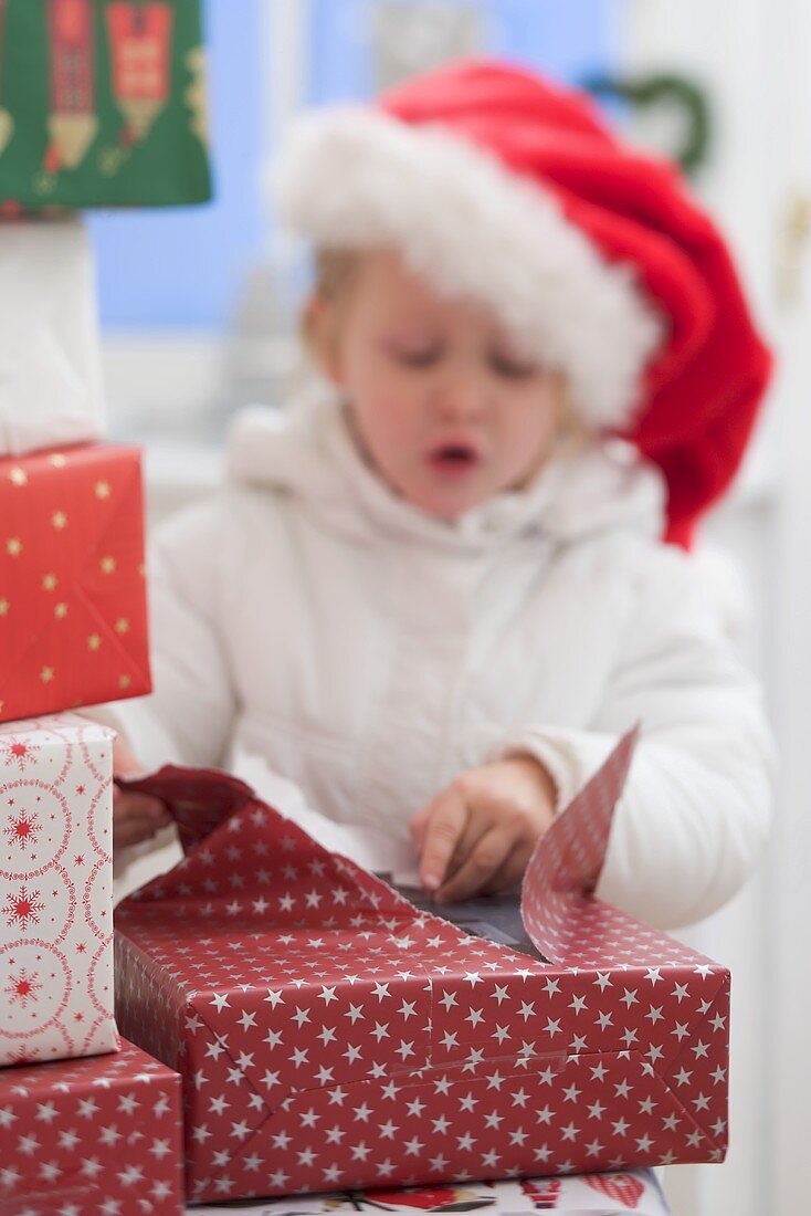 Child in Father Christmas hat opening Christmas parcel