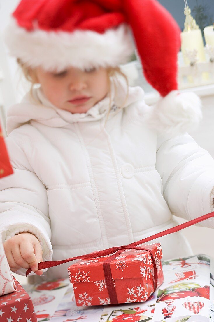 Small girl in Father Christmas hat opening Christmas parcel