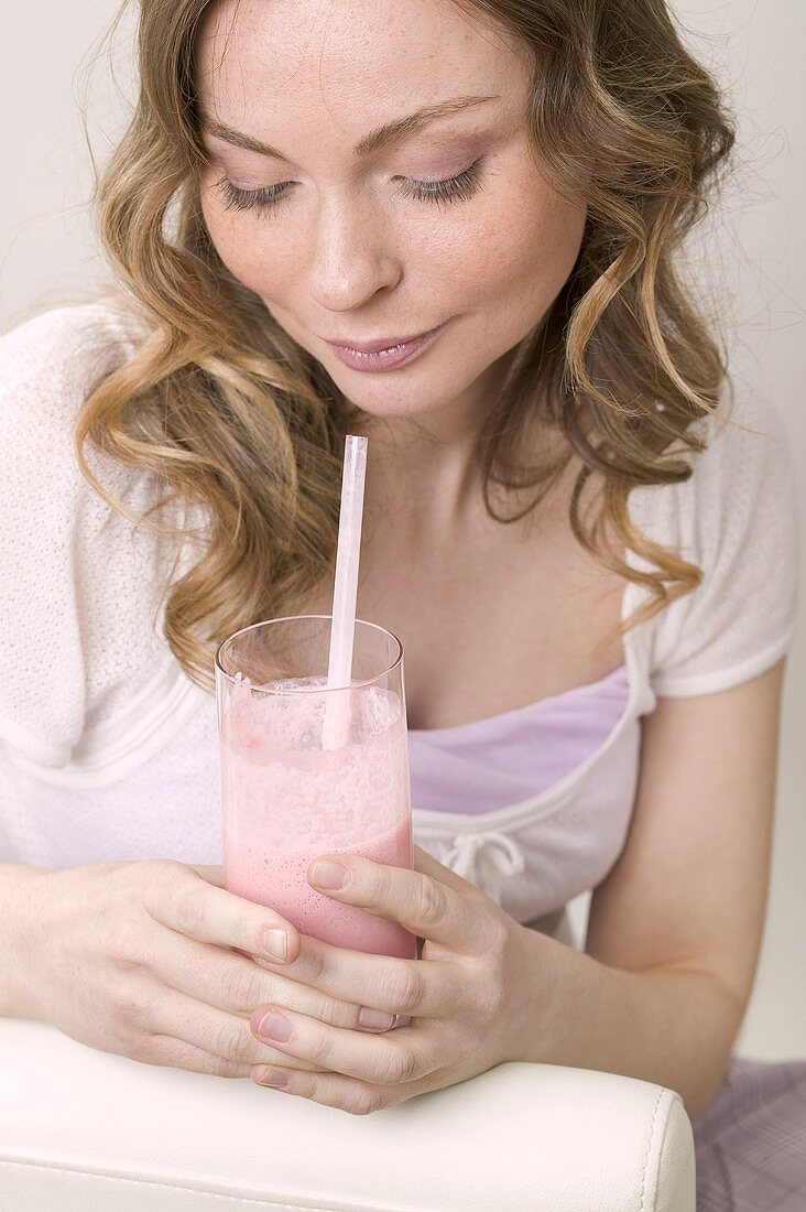 Woman holding glass of strawberry shake with straw