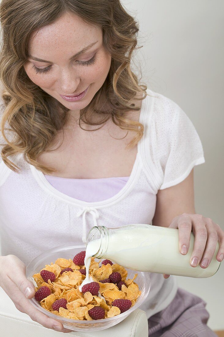 Frau giesst Milch auf Cornflakes mit Himbeeren