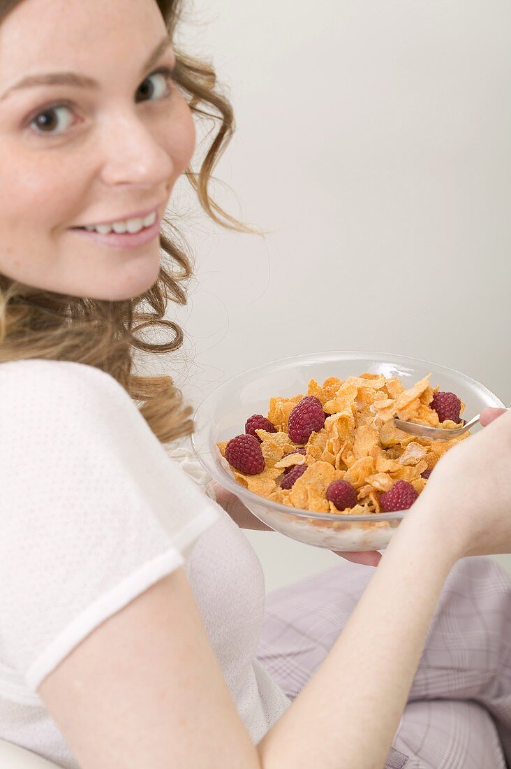 Frau isst Cornflakes mit Himbeeren