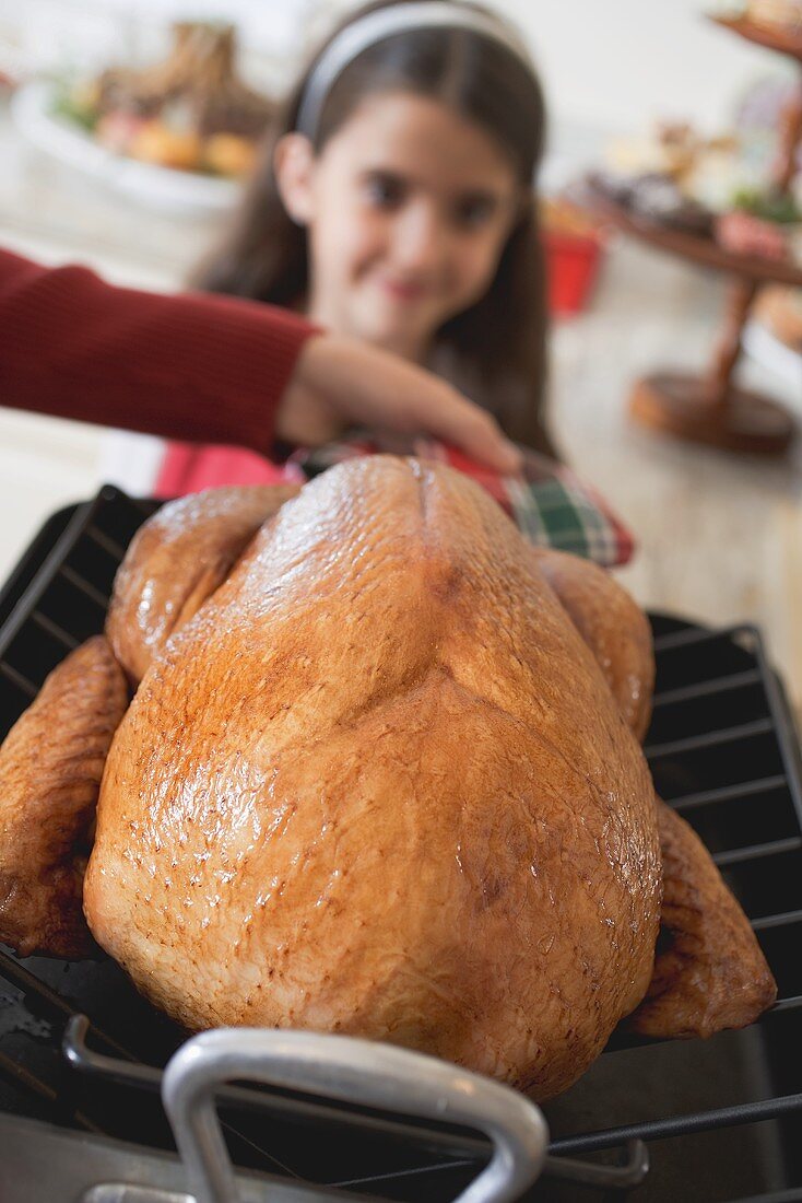 Woman holding turkey in roasting dish, girl in background