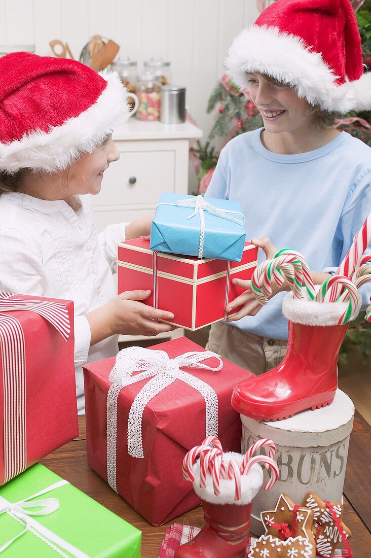 Mädchen und Junge mit Weihnachtsmützen überreichen Geschenke