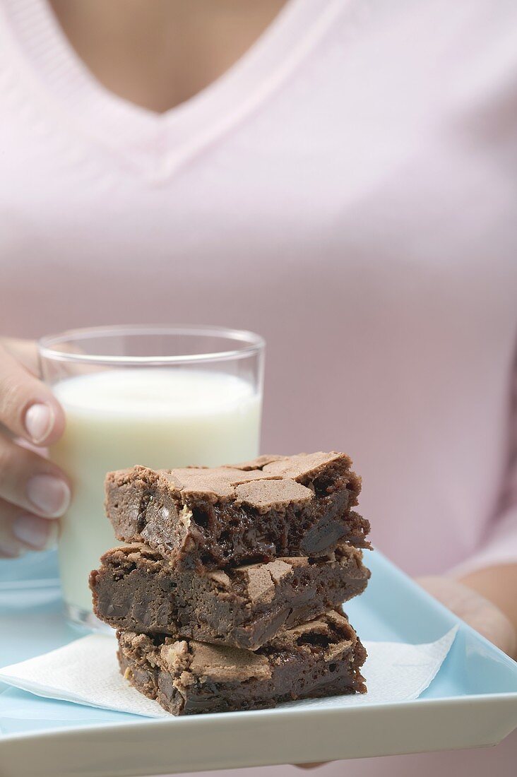 Frau hält Brownies und Glas Milch auf quadratischem Telller