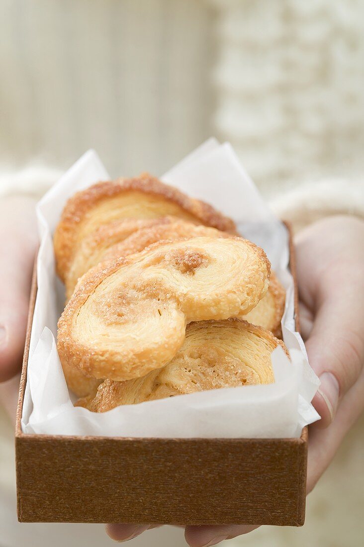 Hands holding palmiers (puff pastry biscuits) in box