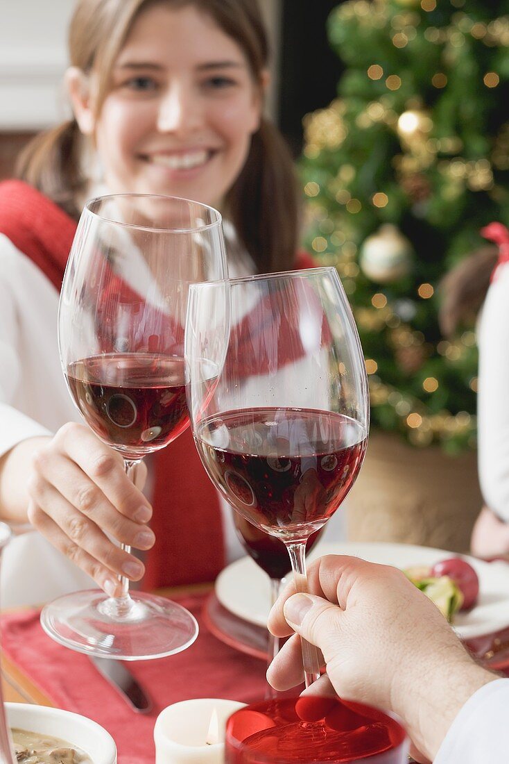 Junge Frau stösst mit Rotweinglas an beim Weihnachtsessen