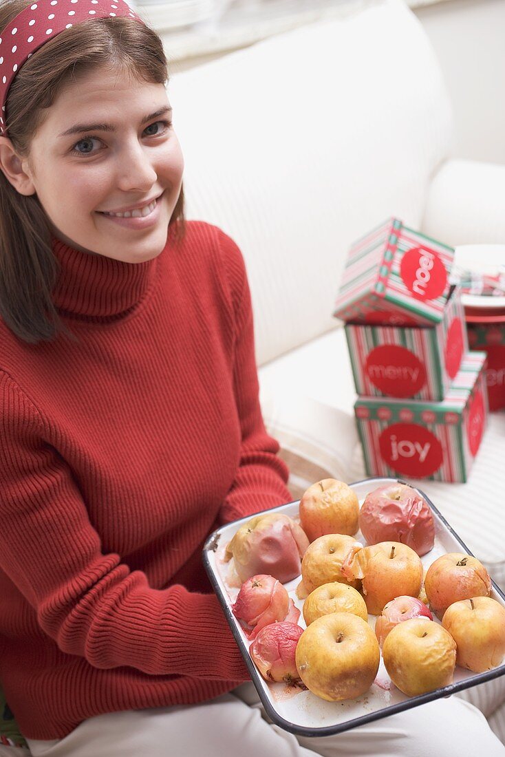 Young woman holding baked apples on baking tray