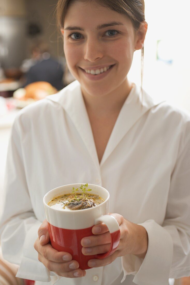 Junge Frau hält Tasse mit Champignonsauce