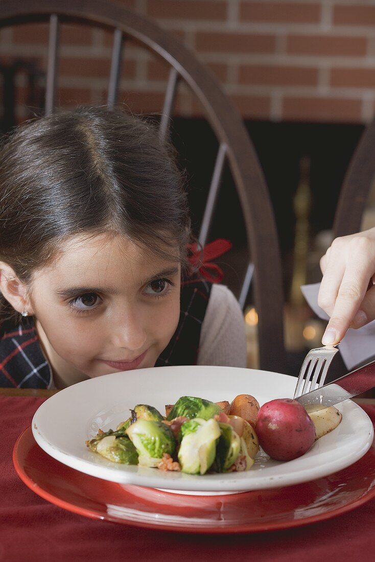 Hand zerteilt für kleines Mädchen Gemüse am Teller