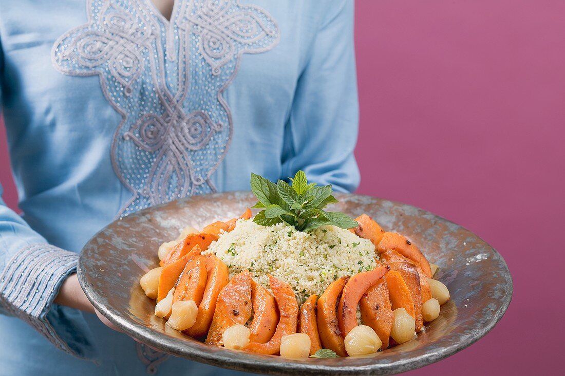 Woman serving couscous with pumpkin, mint and onions