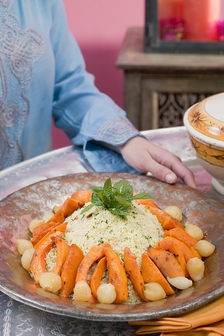 Frau serviert Couscous mit Kürbis, Minze und Zwiebeln