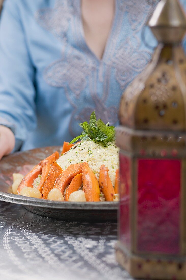 Woman serving couscous with pumpkin, mint and onions